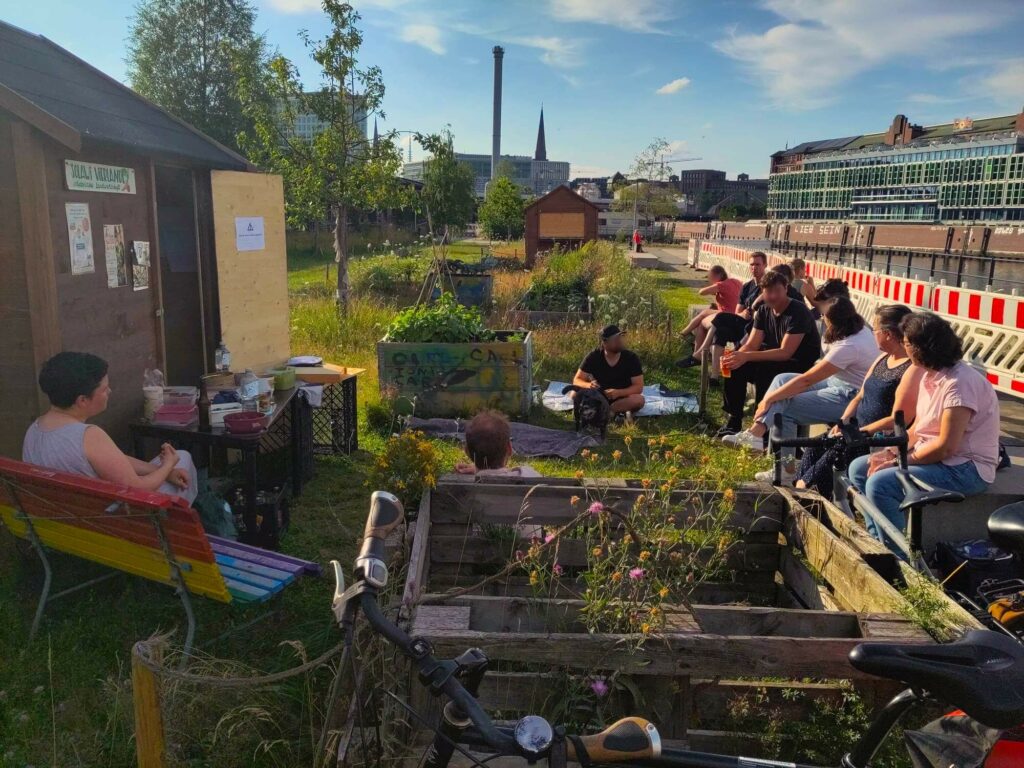 Eine Gruppe von Menschen vor dem Depot im Oberhafen Garten. Die Abendsonne scheint. Im HIntergrund ist der Großmarkt und die Skyline von Hamburg City zu sehen.