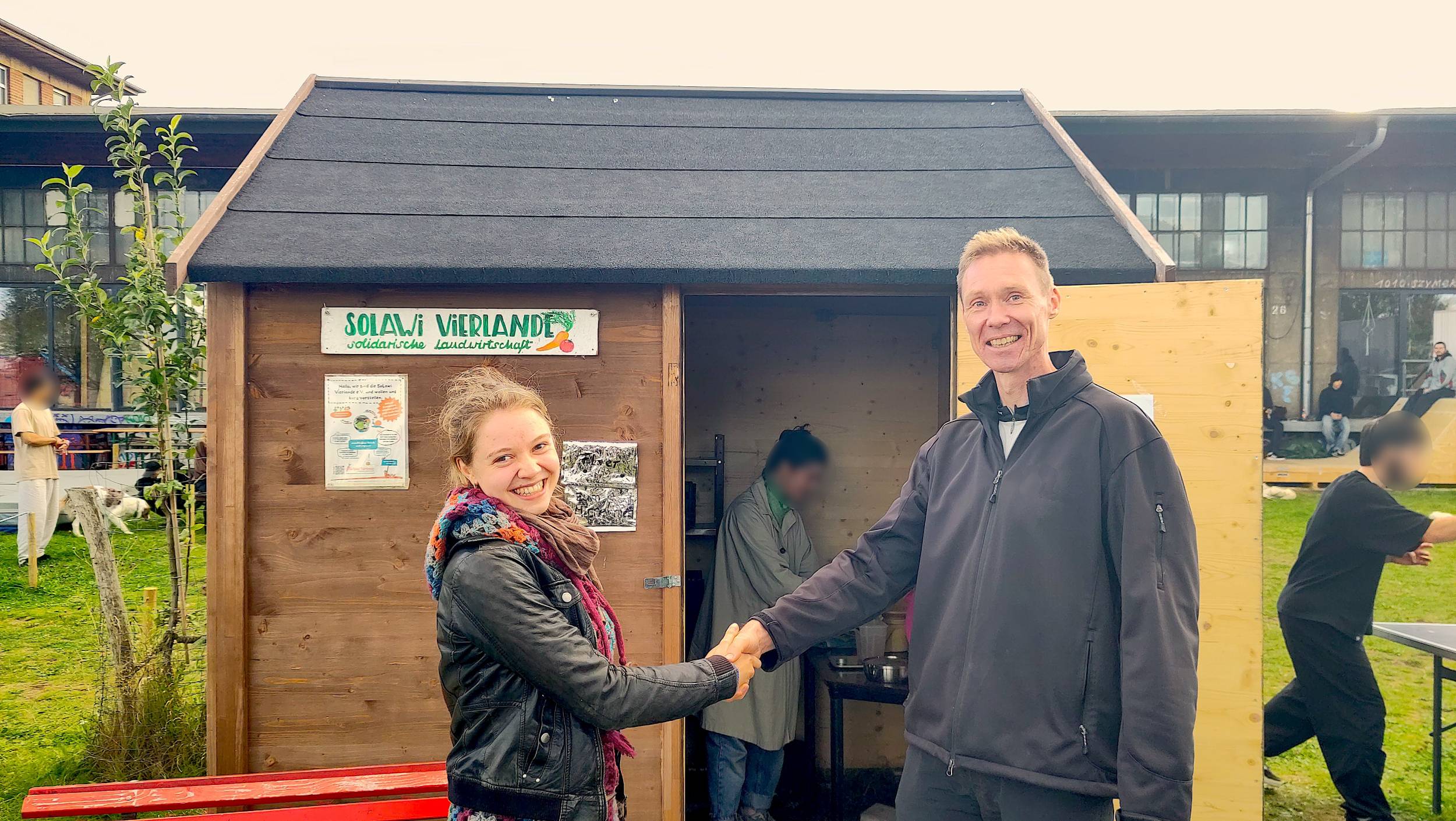 Ina von der SoLawi Ginsterbusch und Carsten von der SoLawi Vierlande stehen vor dem Depot im Oberhafen und geben sich die Hand.